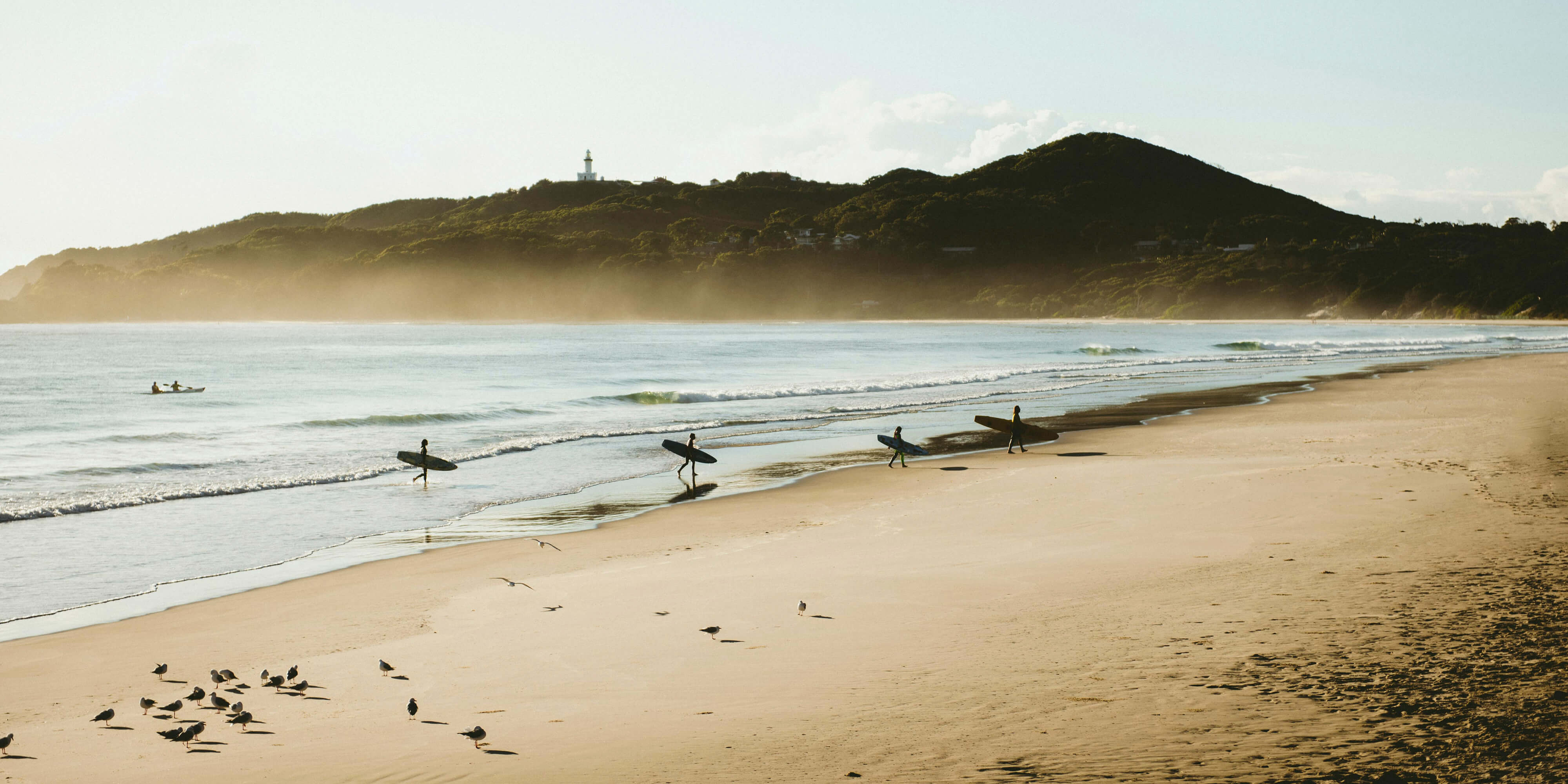 4 surfers coming out of the ocean at sunrise with hills in the background