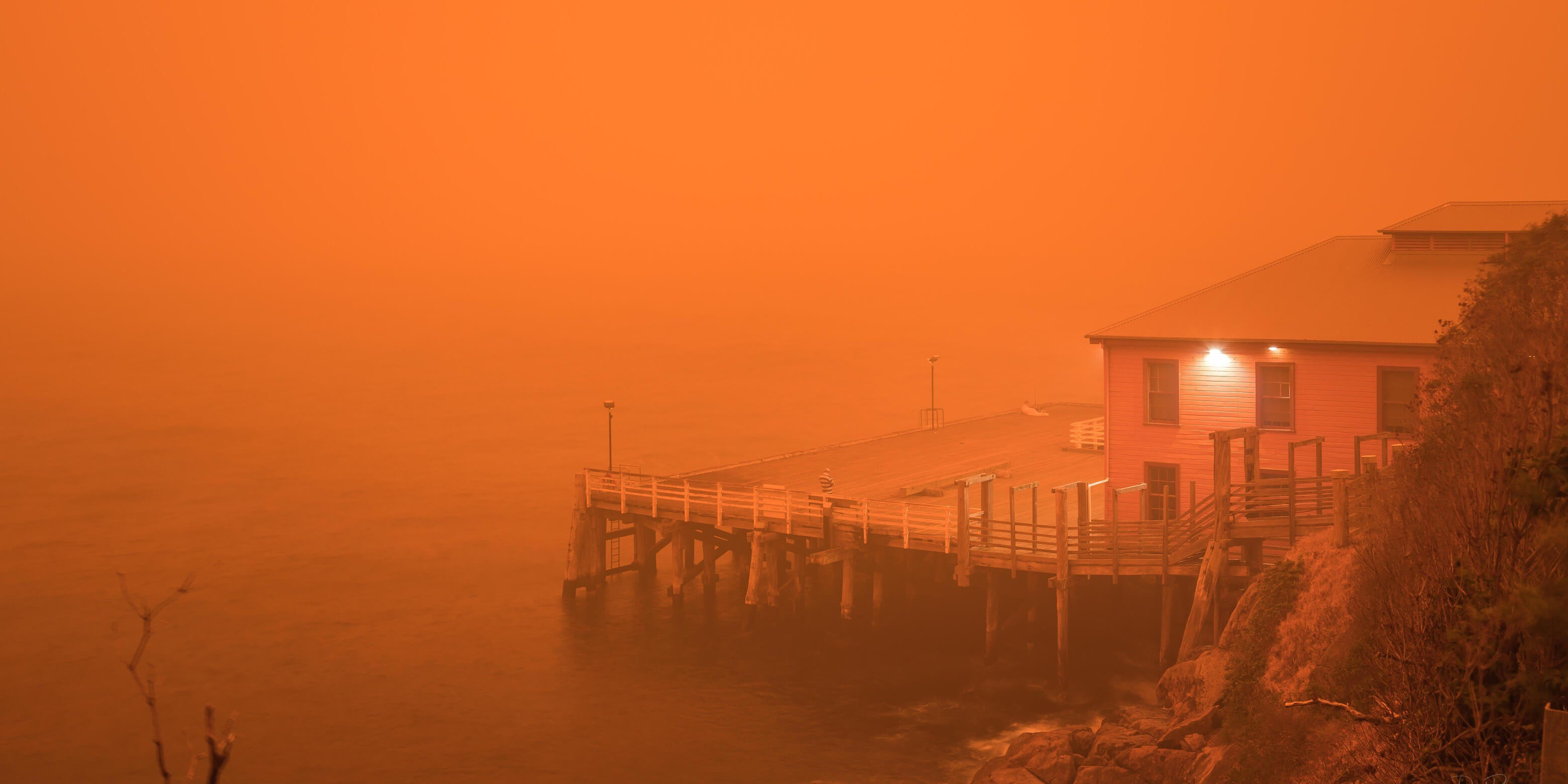 A wharf and building next to the building. Everything in the image is glowing in bright orange due to bushfires near by 