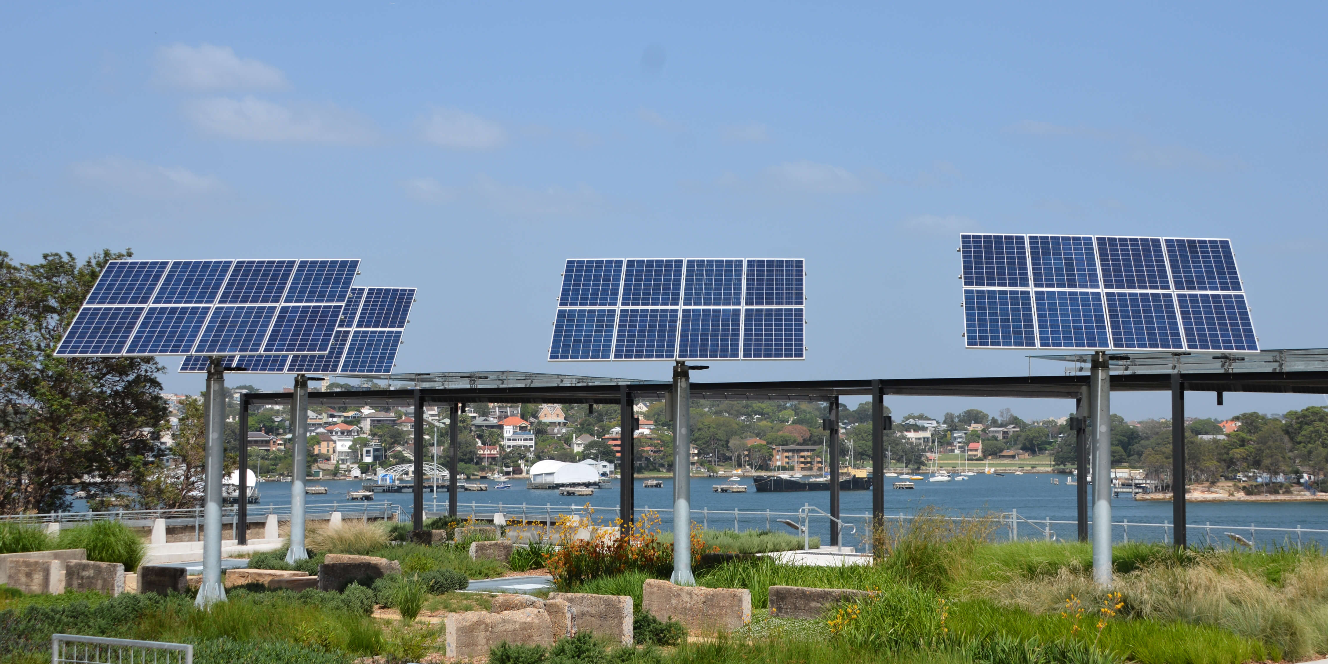 Four large solar panels located in a community garden with Sydney Harbour in the background